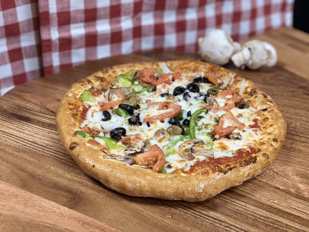 Close up shot of Manny & Olga’s vegetarian pizza with fresh sliced tomatoes, onions, green peppers, black olives, mushrooms, green olives & extra cheese.

