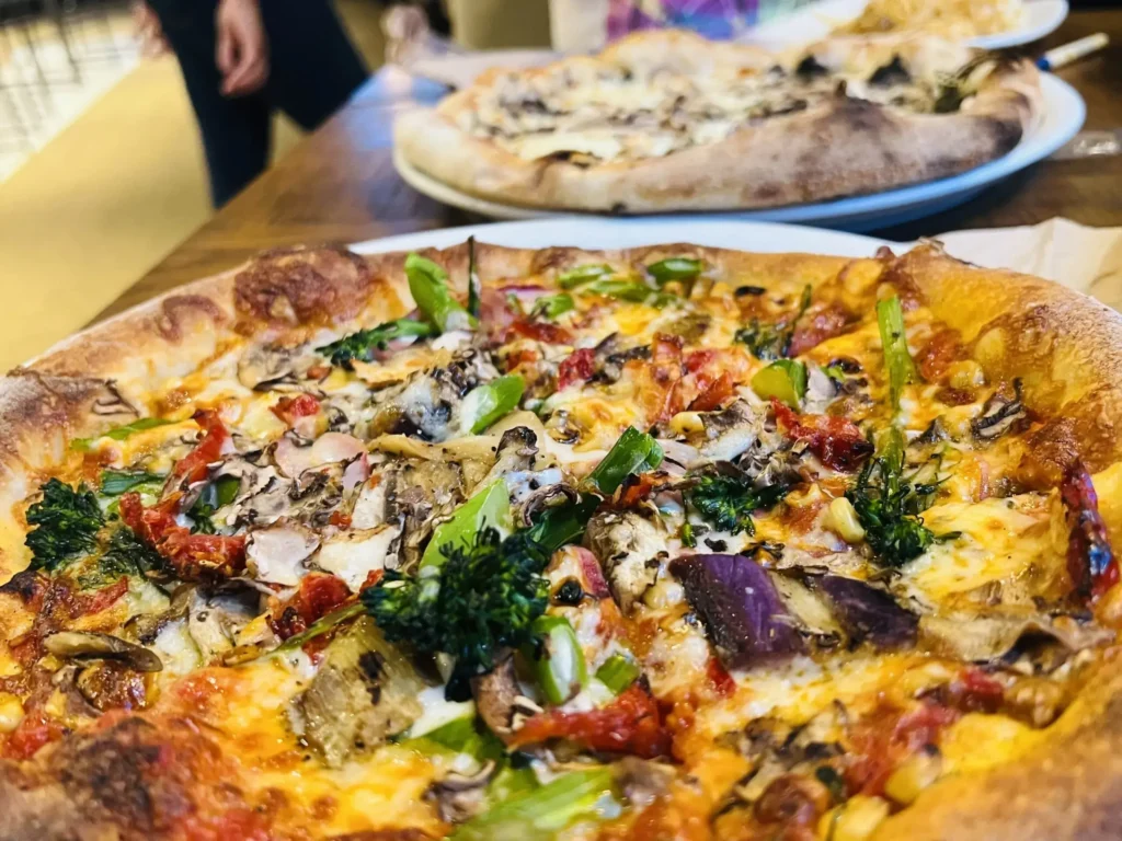 A vibrant pizza with mushrooms, broccoli, sun-dried tomatoes, and other vegetables.