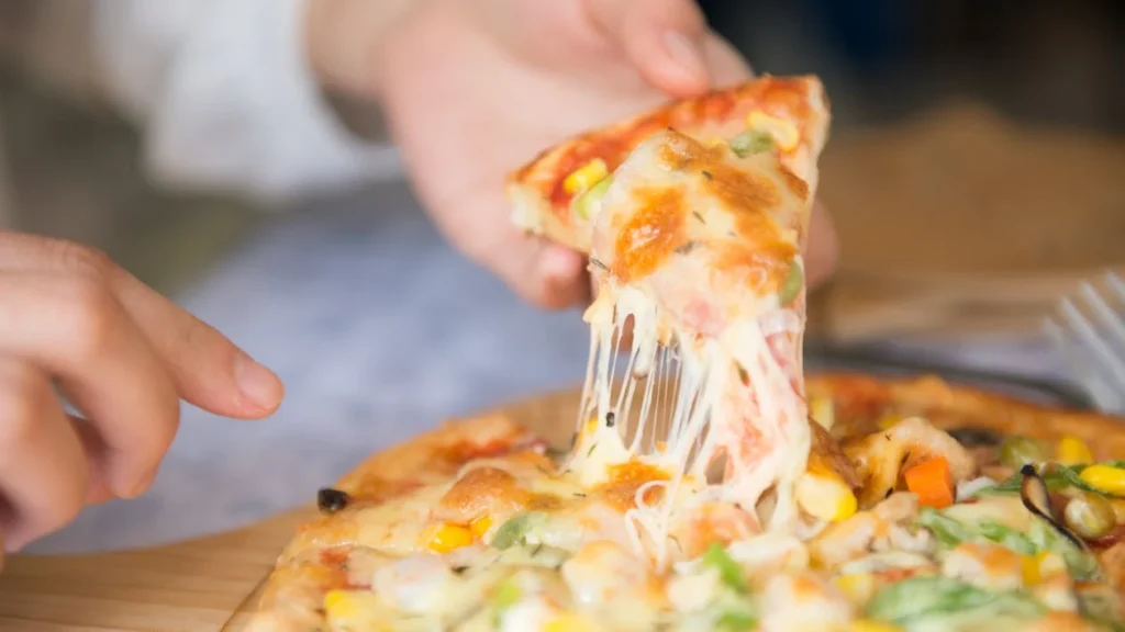 Close-up shot of a cheesy slice of pizza from a whole sea-food pizza.
