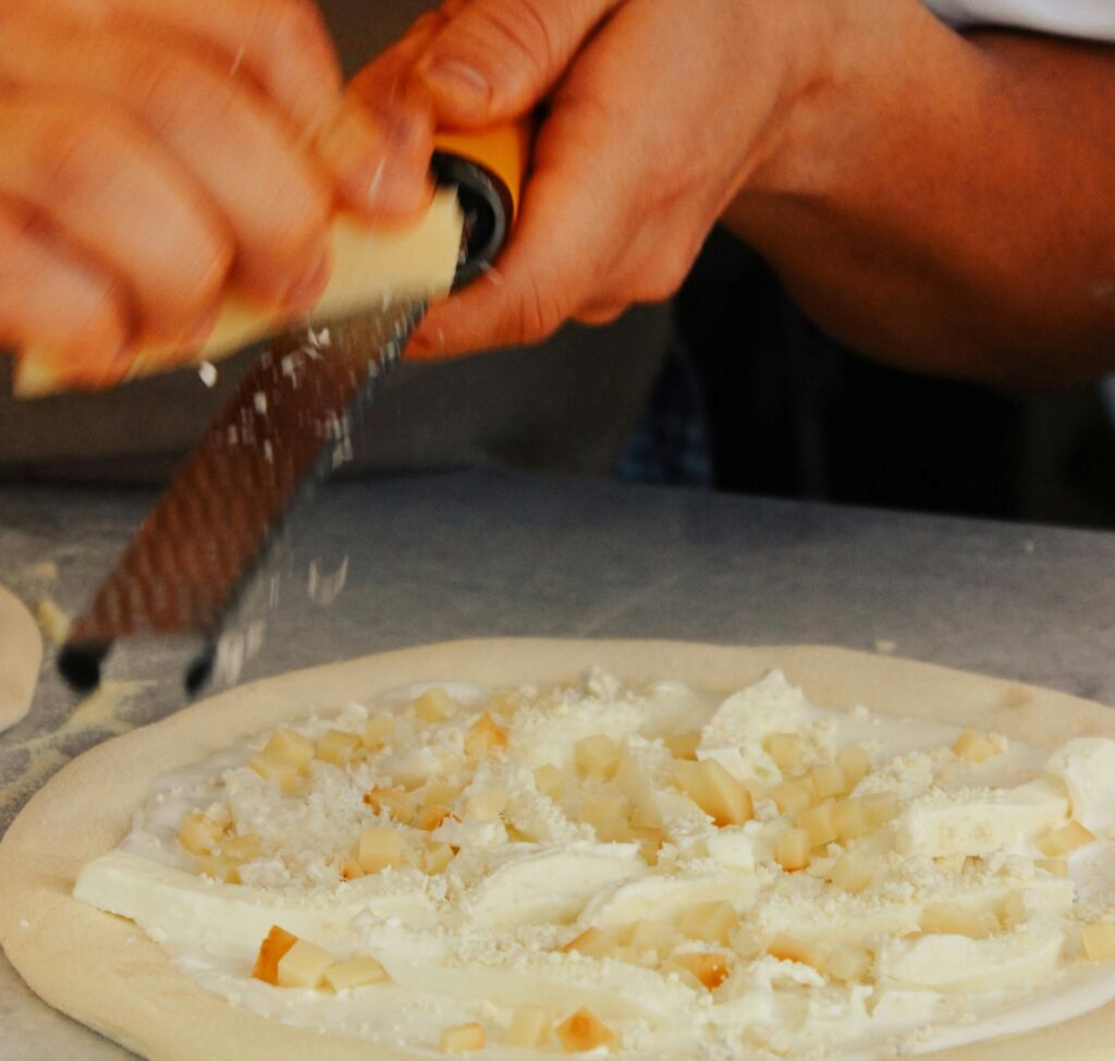 A chef grates cheddar cheese on top of pizza dough.
