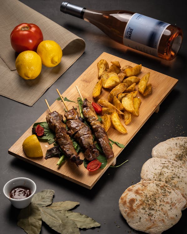 Flame-grilled Chicken Souvlaki skewers with potato wedges, fresh bread, and a glass of wine at Manny & Olga’s.