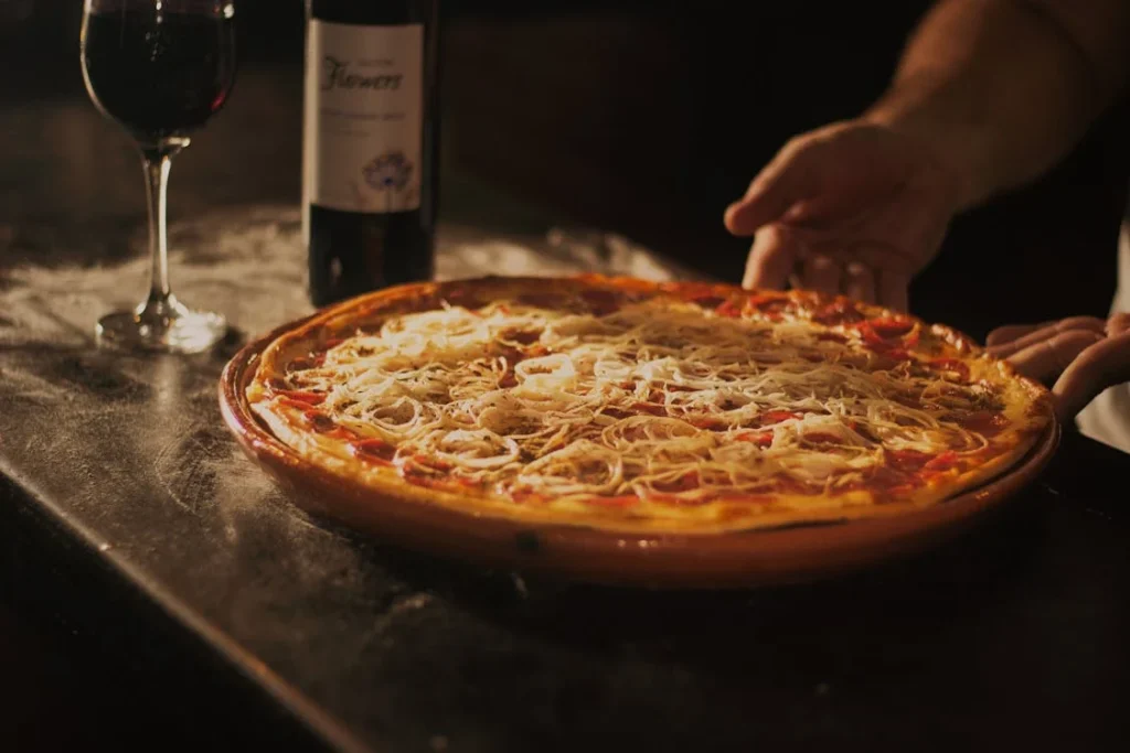 Close-up shot of pepperoni pizza with extra cheese on top, with a glass of wine on the side.
