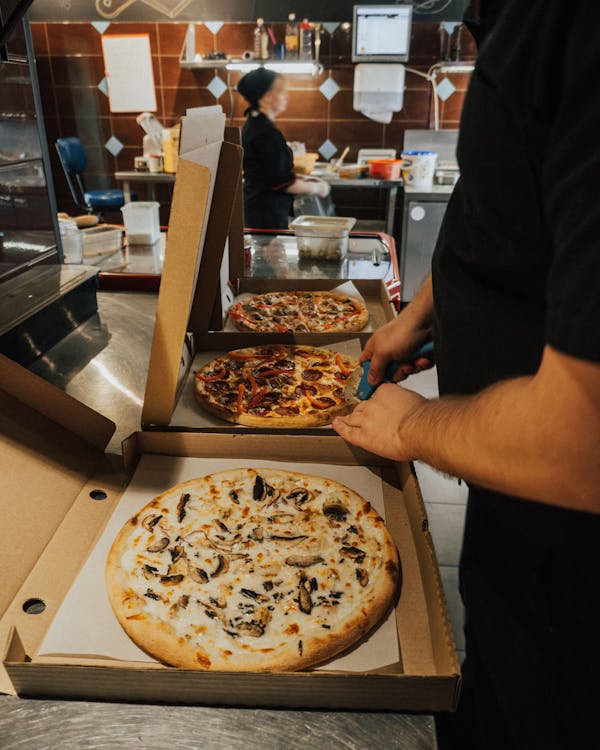 A person slices pizza in different boxes.