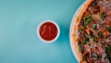 A flat-lay shot of a meat pizza paired with a spicy dipping sauce, showcasing a bold flavor combination.